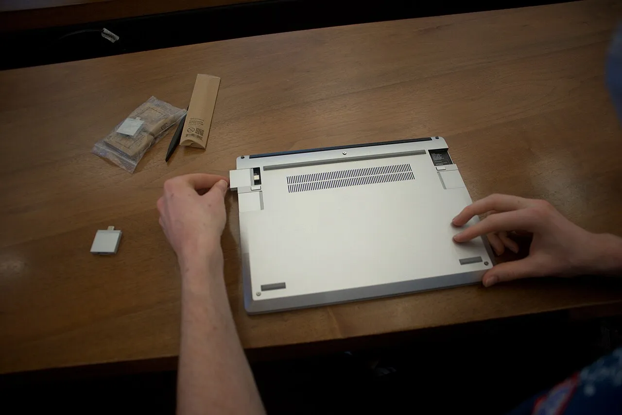 Framework Desktop mini-PC being assembled on a wooden desk, the open silver chassis showing the mainboard and modular internals.
